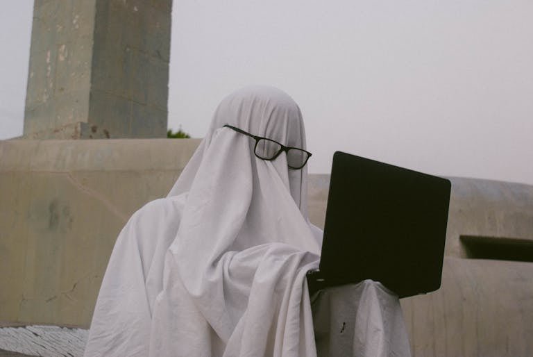 A humorous depiction of a person in a ghost costume using a laptop - a literal ghostwriter