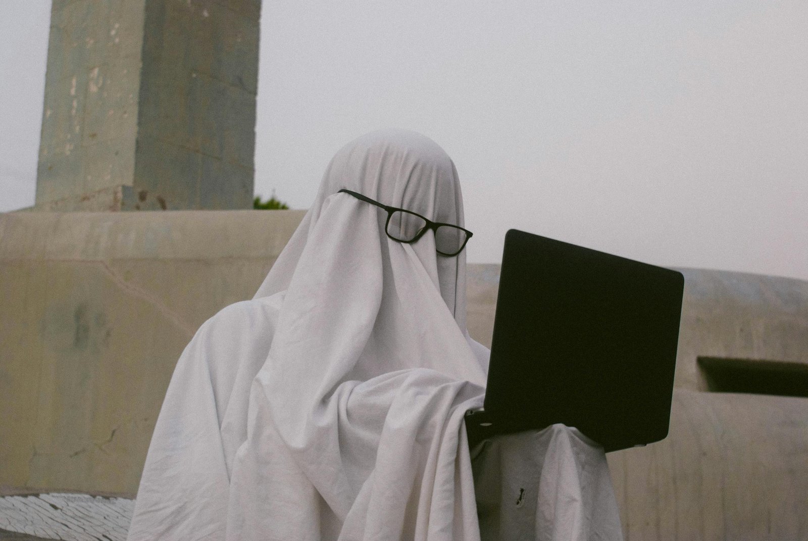 A humorous depiction of a person in a ghost costume using a laptop - a literal ghostwriter
